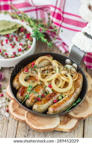 Fried sausages with spices and onions in a frying pan on wooden table