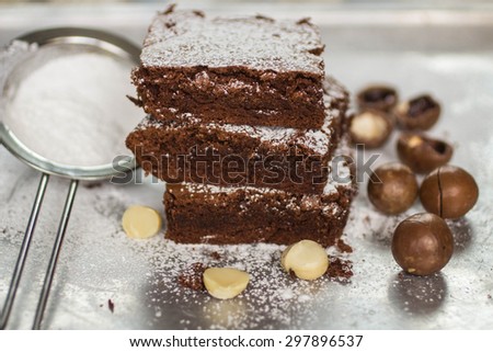Brownie. Chocolate cakes with powdered sugar and macadamia on a metal baking sheet.  American dish.  Selective focus