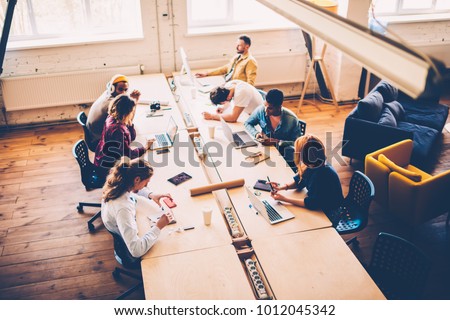 Top view of multiracial group of students have training lesson in classroom using technology, crew of creative designers collaborating during brainstorming session in coworking office sitting at table