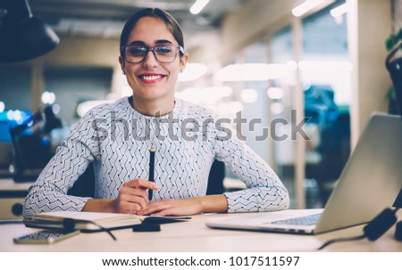 Portrait of cheerful businesswoman satisfied with occupation sitting at desktop in office with modern technologies,smiling female designer happy about accomplished creative project looking at camera