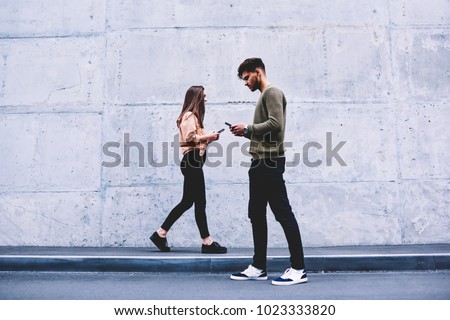 Male and female hipsters walking on grey wall background ignoring each other preferring social networks,students chatting online instead of communicating in real life strolling pon publicity area