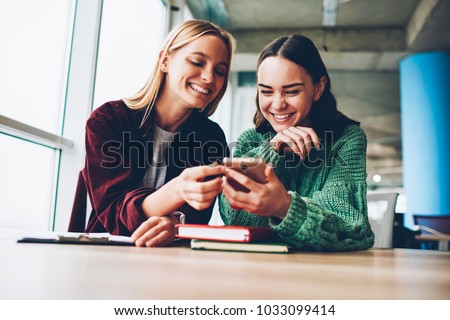 Happy best friends laughing during watching funny videos on internet websites enjoying social media life during break.Two cheerful female bloggers reading positive comments on smartphone device