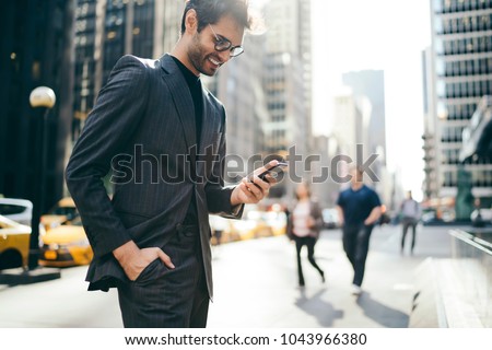 Cheerful male trader dressed in elegant suit laughing while reading good business news on internet website on smartphone.Happy businessman received notification of high financial balance on cellular