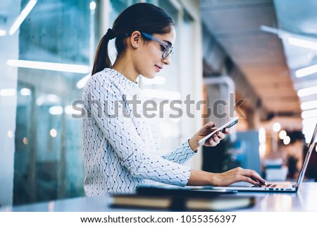 Skilled female receptionist checking notification of mails on cellphone working with laptop computer at desk,professional administrative manager of office using app for organizing data on technologies