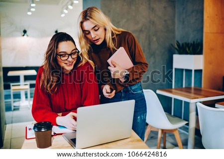 Skilled female students making research on laptop computer doing homework in college campus,hipster girls communicating in university library watching training webinar together on netbook for learning