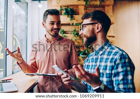 Successful male startuppers discussing plan together for work smiling and gesturing, happy hipster guys having friendly conversation about business information having meeting in coworking office