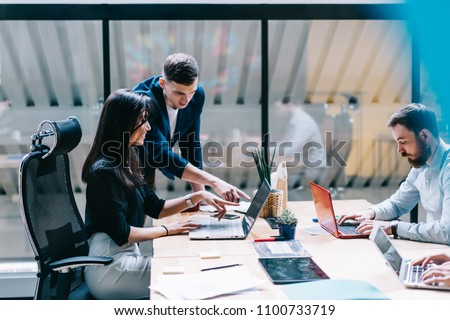Proud ceo pointing on laptop computer and discussing graphic presentation made by creative female designer during working process in IT company.Office employees using laptops and internet connection