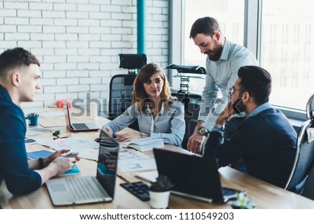 Male and female colleagues discussing working strategy of cooperation having briefing meeting in office.Team of employees in formal wear collaborating with each other sitting at table with laptops