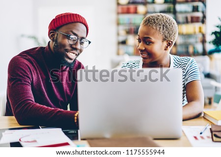 African american couple browse website on laptop computer making shopping online together at home interior, positive dark skinned hipster guy showing new app for netbook sitting at his girlfriend