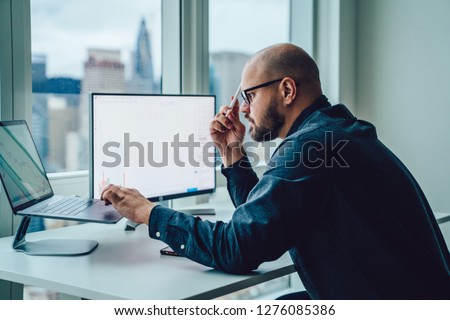 Back view of businessman sitting at office desktop front PC laptop computers with financial graphs and statistics on monitor.Making research, analysis of digital market and investment in block chain