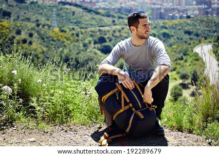 Young tourist on a halt resting holding his travel backpack and looking away