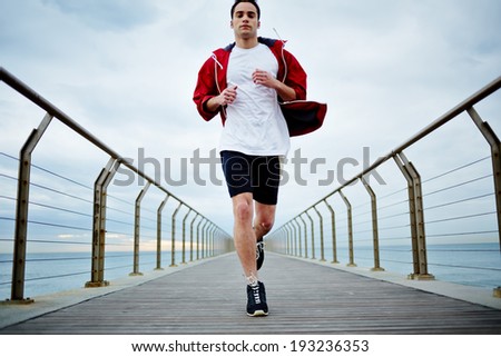Full length portrait of sporty guy running fast along beautiful pier