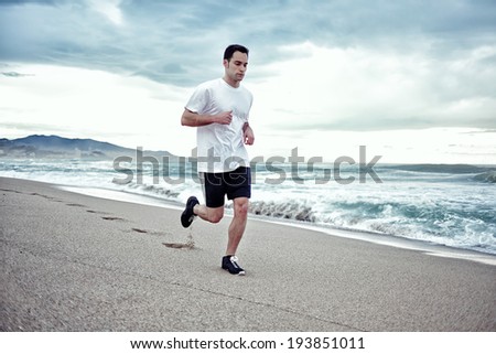 Young athlete man in white t-shirt runs on the beach enjoying the beautiful sea, HDR effect