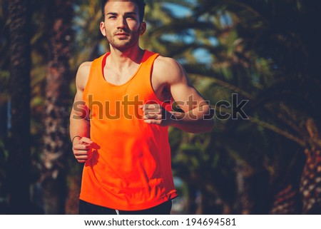 Muscular athletic man in the bright sportswear running on the jogging track and looking at the camera