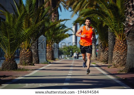 Muscular athletic man in the bright sportswear running on the jogging track
