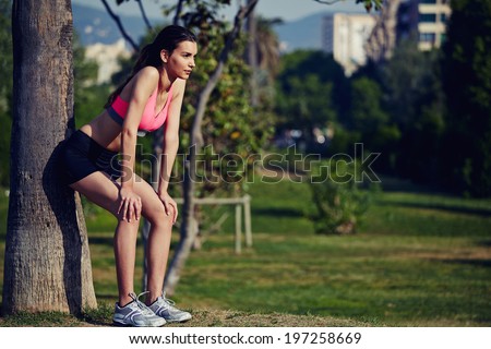 Female runner leaned back against a tree tired after jogging