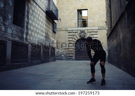 Very charming athlete tired after the morning jog with his hands resting on his knees