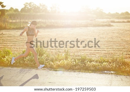 Female jogger runs along a road through the sun\'s rays