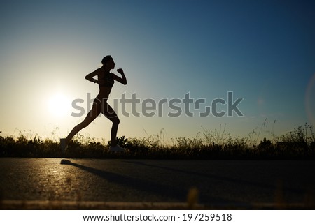 Silhouette of muscular women running on the road at sunset