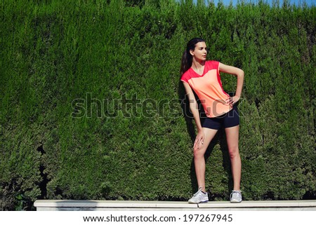 Beautiful young model dressed in sportswear posing against natural green background-copy space with fashion colors