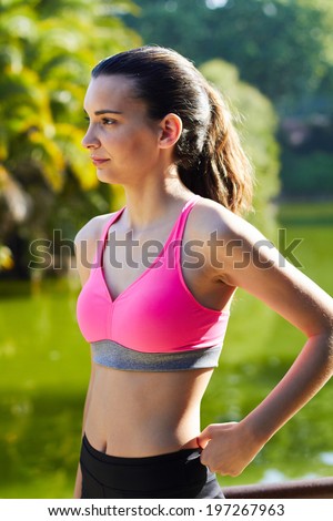 Portrait of beautiful young woman dressed in sportswear taking a break after run, charming fit girl resting after workout in sunny park