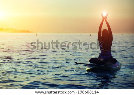 Silhouette of a girl holding sun in the hands on sup yoga meditation, harmony with the nature in yoga meditation during beautiful dawn