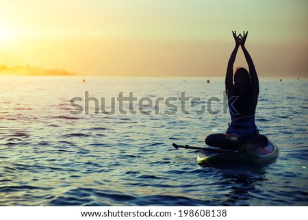 Harmony with the nature in yoga meditation, silhouette of a girl doing sup yoga at the beautiful orange sunset