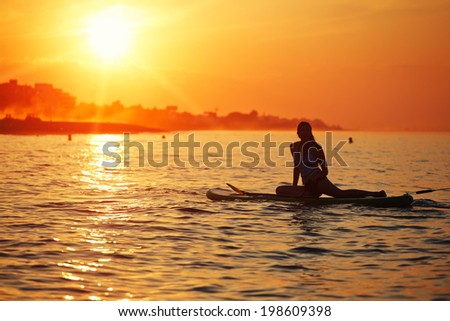 Silhouette of a girl floating on the sea with surf board on the excellent background of orange sunset