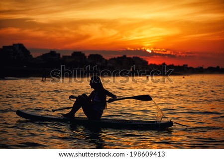 Silhouette of a girl floating on the sea with surf board on the excellent background of orange sunset