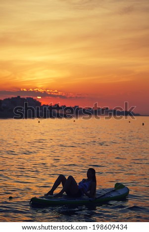 Beautiful woman engage paddle surf yoga at the amazing sunset over the sea, spiritual yoga meditation on the beach
