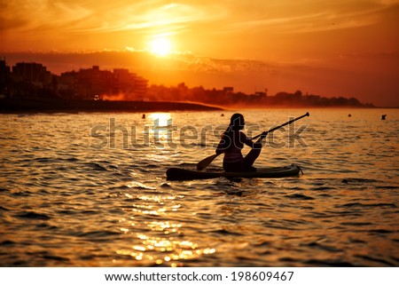 Silhouette of a beautiful girl floating at sea on paddle surf board encountering stunning sunrise reflected on the Gulf Indian Ocean