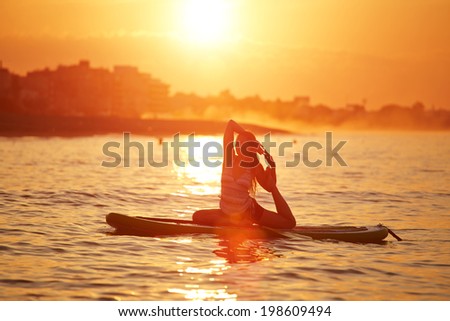 Harmony with the nature in yoga meditation, silhouette of a girl doing sup yoga at the beautiful orange sunset reflected on the sea