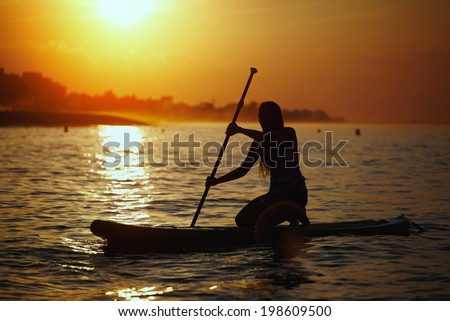 Accompanied by a stunning sunset beautiful girl floats on surf board, sup yoga training