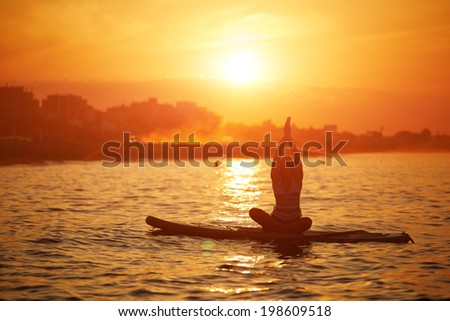 Harmony with the nature in yoga meditation, silhouette of a girl doing paddle board yoga at the beautiful orange sunset reflected on the sea