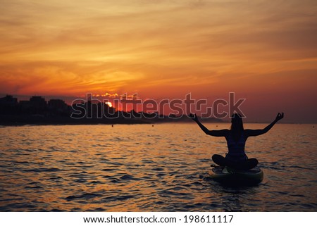 Silhouette of a beautiful girl engage paddle board yoga at the perfect orange sunset over the ocean, spiritual yoga meditation on the beach