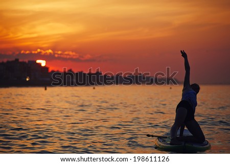 Beautiful silhouette of a girl engage paddle board yoga at the perfect orange sunset over the ocean