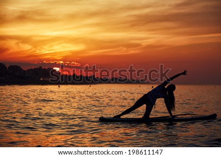 Fine and perfect silhouette of a girl engage paddle surf yoga at the amazing sunset over the sea, harmony with the nature in yoga meditation