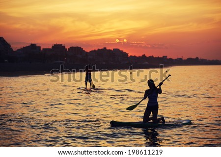 Silhouettes of perfect couple engage standup paddle boarding and meets dawn in the Gulf of Indian Ocean, the perfect orange sunset over the ocean
