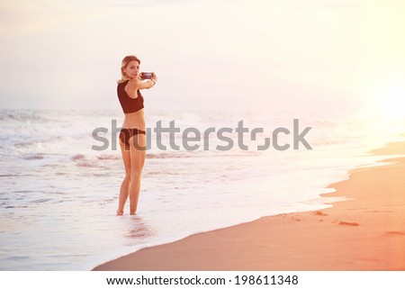 Walk by the sea, girl photographing a beautiful sunny sunset standing in the sea