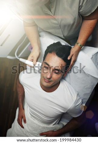 Handsome male patient in white t-shirt having a laser skin treatment in a skincare clinic, male patient on the rejuvenation procedure in aesthetic clinic, laser procedure