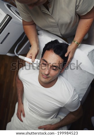 Beautiful man with closed eyes having a laser skin treatment in a skincare clinic, male patient lying on the medical chair at rejuvenation procedure in aesthetic clinic