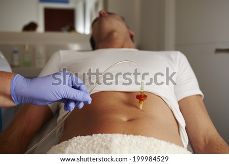 Beautiful man at abdomen mesotherapy gun therapy lying on the medical chair in the cabinet of aesthetic clinic