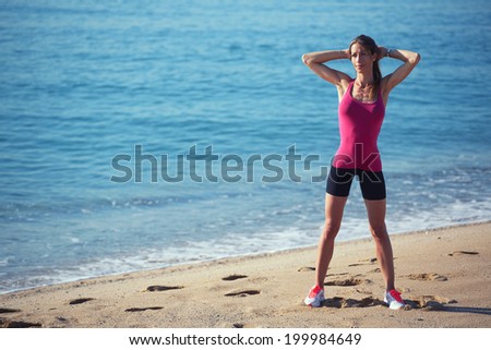 Slim sports woman dressed in pink t-shirt and black shorts doing workout before the morning jog along the sea