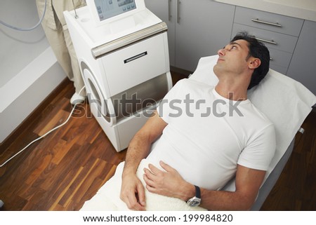 Handsome male patient dressed in white shirt lying in the medical cabinet of aesthetic clinic