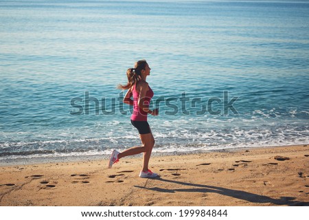 Beautiful female jogger runs along the sea at sunny morning, sports woman runs leaving footprints on the sand