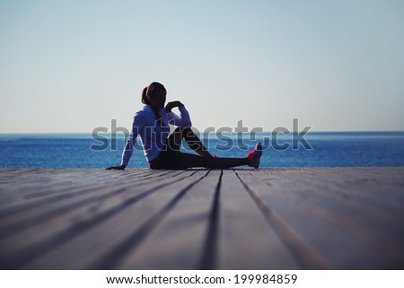 Beautiful athletic woman seated on the wooden pier and resting after the morning intensive jog, beautiful athletic woman seated on the wooden pier on the sea background