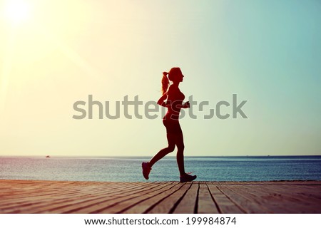 Athletic female runner with a beautiful figure runs on the wooden pier on the sea and sky background, morning jog on the beach