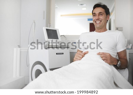 Handsome male patient dressed in white shirt smiling to the doctor seated in the medical cabinet of aesthetic clinic