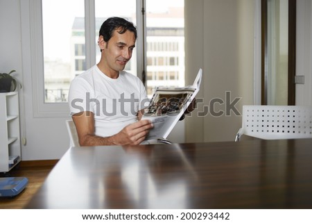 Attractive man reads journal sitting at a table, waiting to the doctor in private clinic