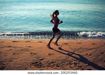 Beautiful female jogger run on the sand along the beach on the the sea background
